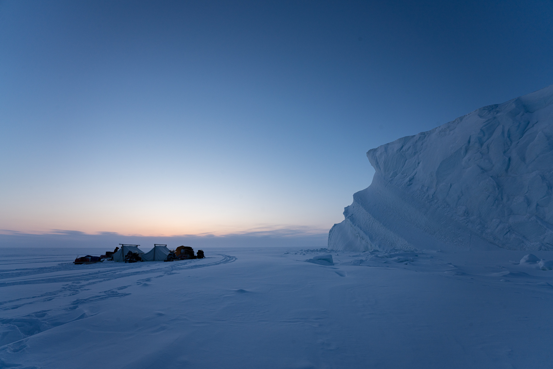Expedition camp at blue hour beneath an iceberg